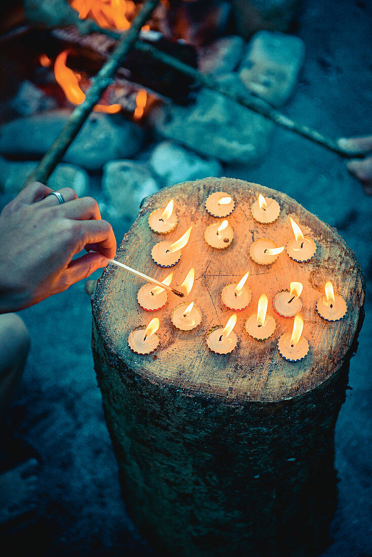 Hand zündet kleine Kerzen in Kronkorken an