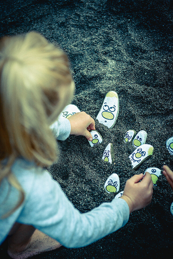 Mädchen spielt mit bunt bemalten Steinen im Sand