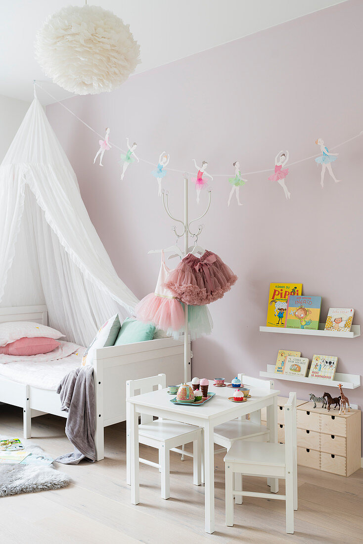 White canopy bed and garland of ballerinas in girl's bedroom with pink walls