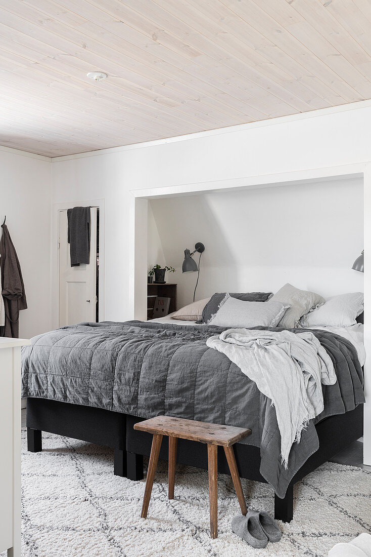 Bed in niche with sloping ceiling in bedroom in shades of grey