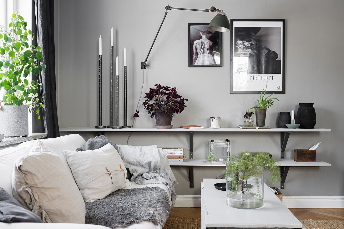 Wohnraum in Grau mit Sofa und niedrigen Wandregalen dekoriert mit Kerzen, Vasen und Pflanzen