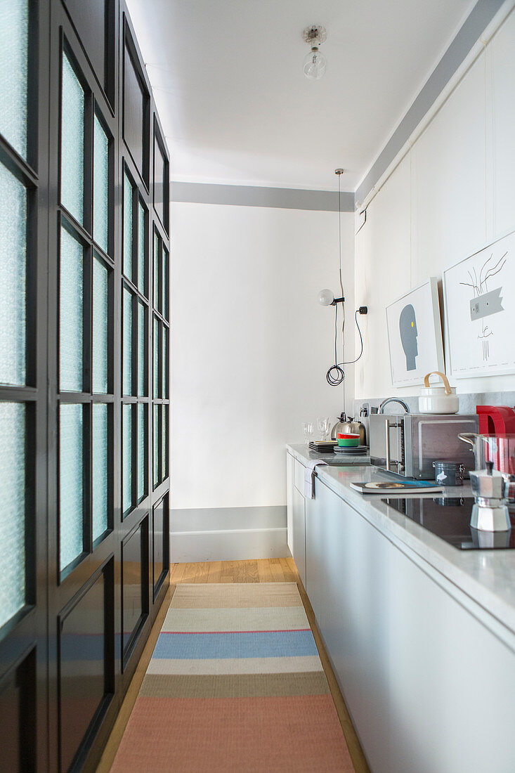Narrow kitchen separated by black lattice and glass partition