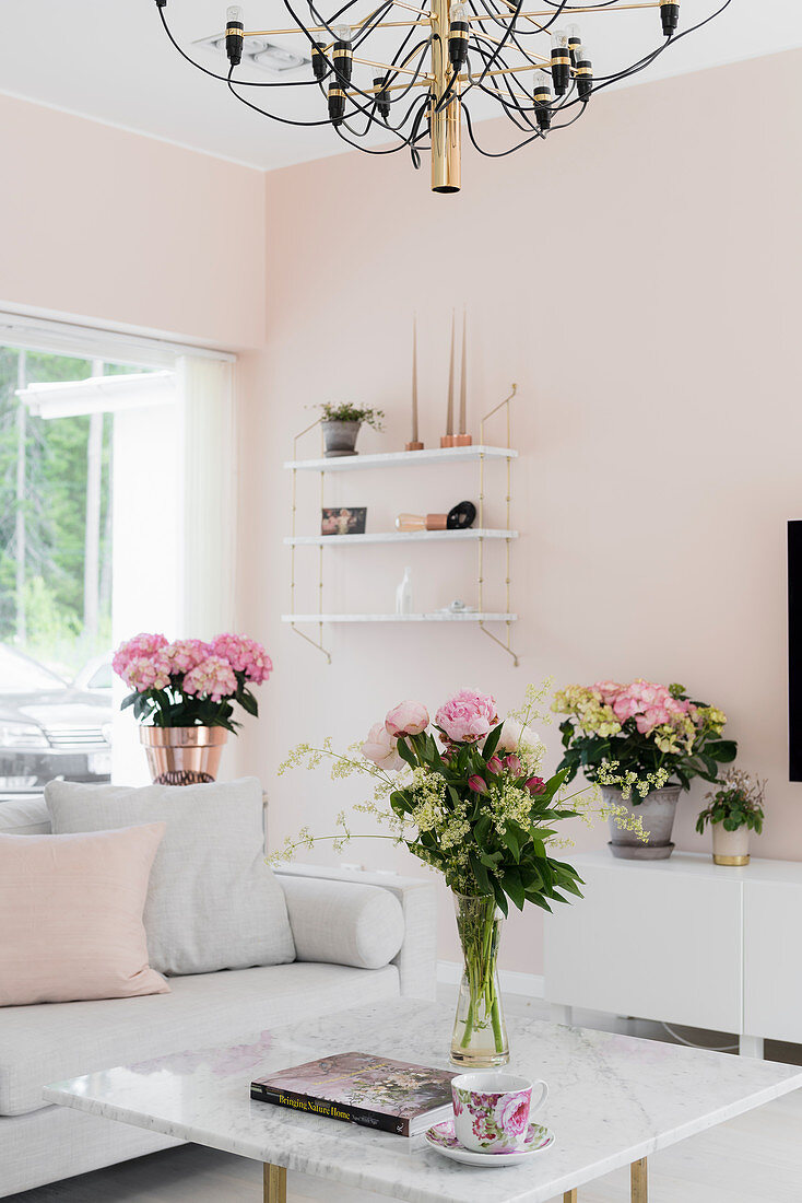 Weiße Möbel und frische Blumen im Wohnzimmer mit kühlen, rosa Wänden
