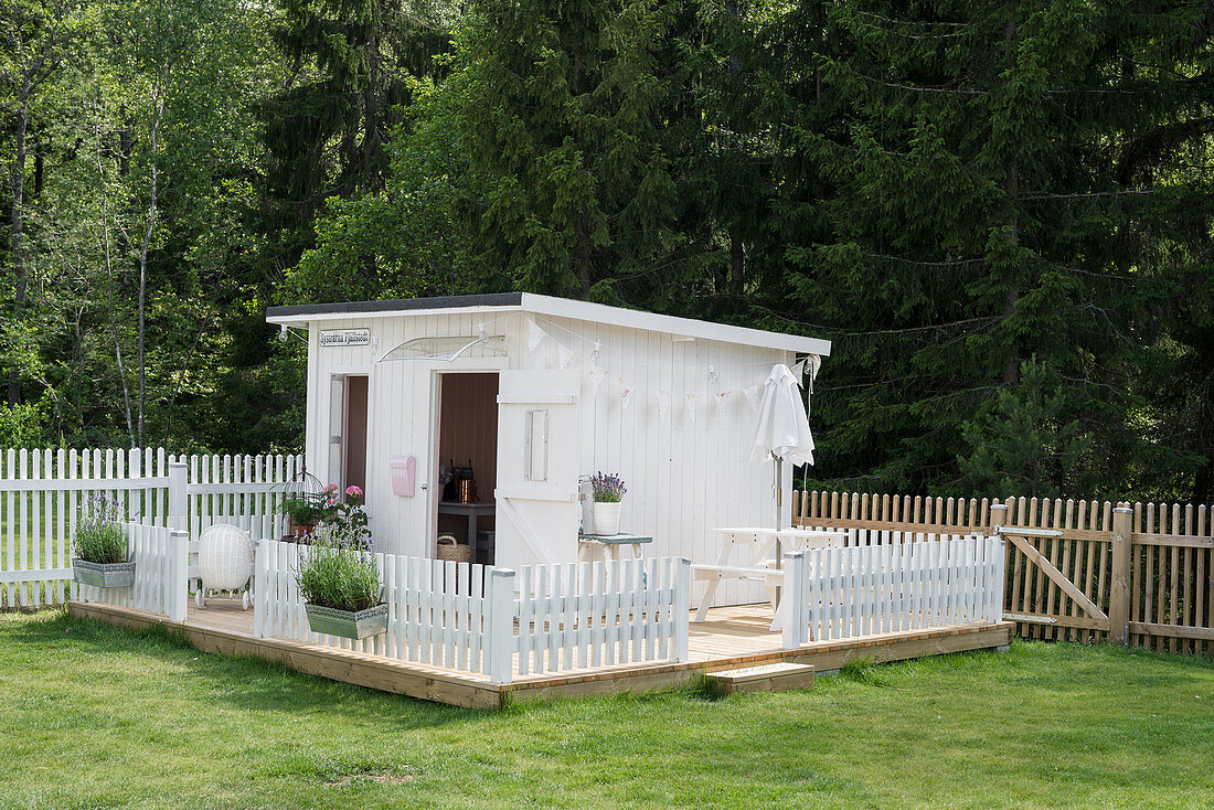 Weißes Spielhaus mit Zaun auf Podest im Garten