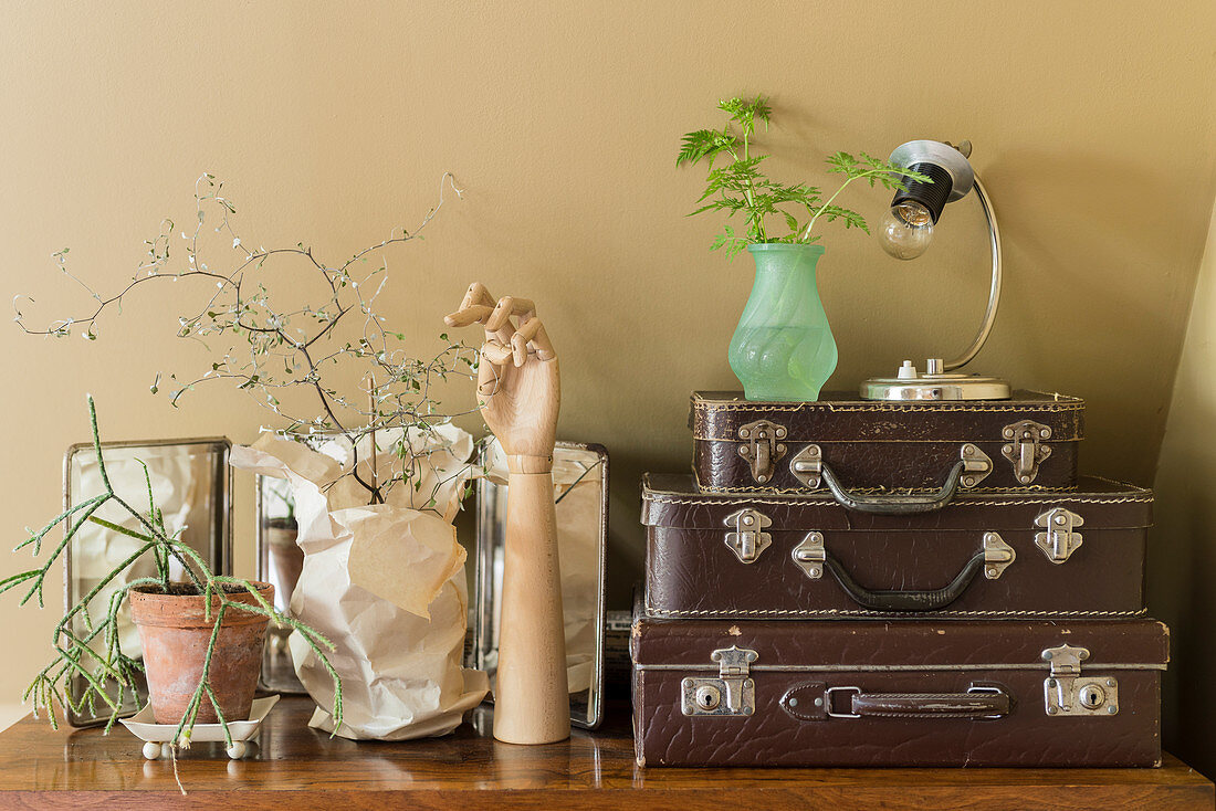 Various ornaments next to stacked vintage cases on top of chest of drawers