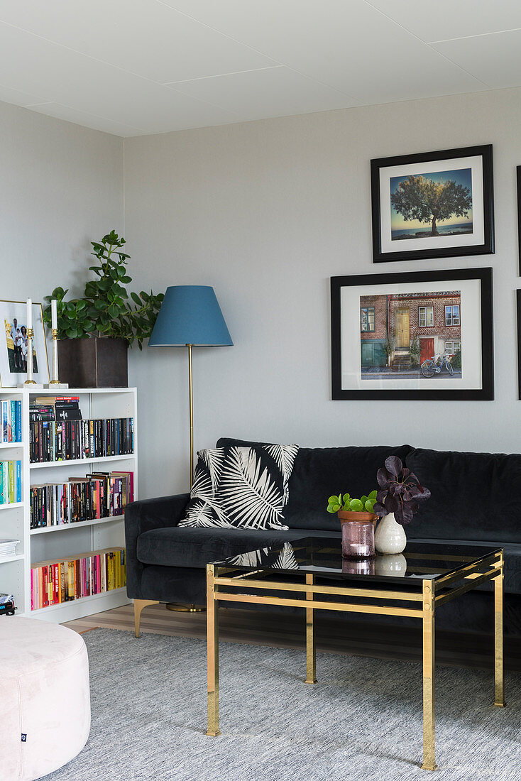 Black velvet couch and brass coffee table next to bookshelves in living room
