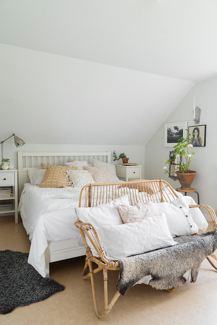 Doppelbett und Rattanbank mit Kissen in weißem Schlafzimmer im Dachgeschoss