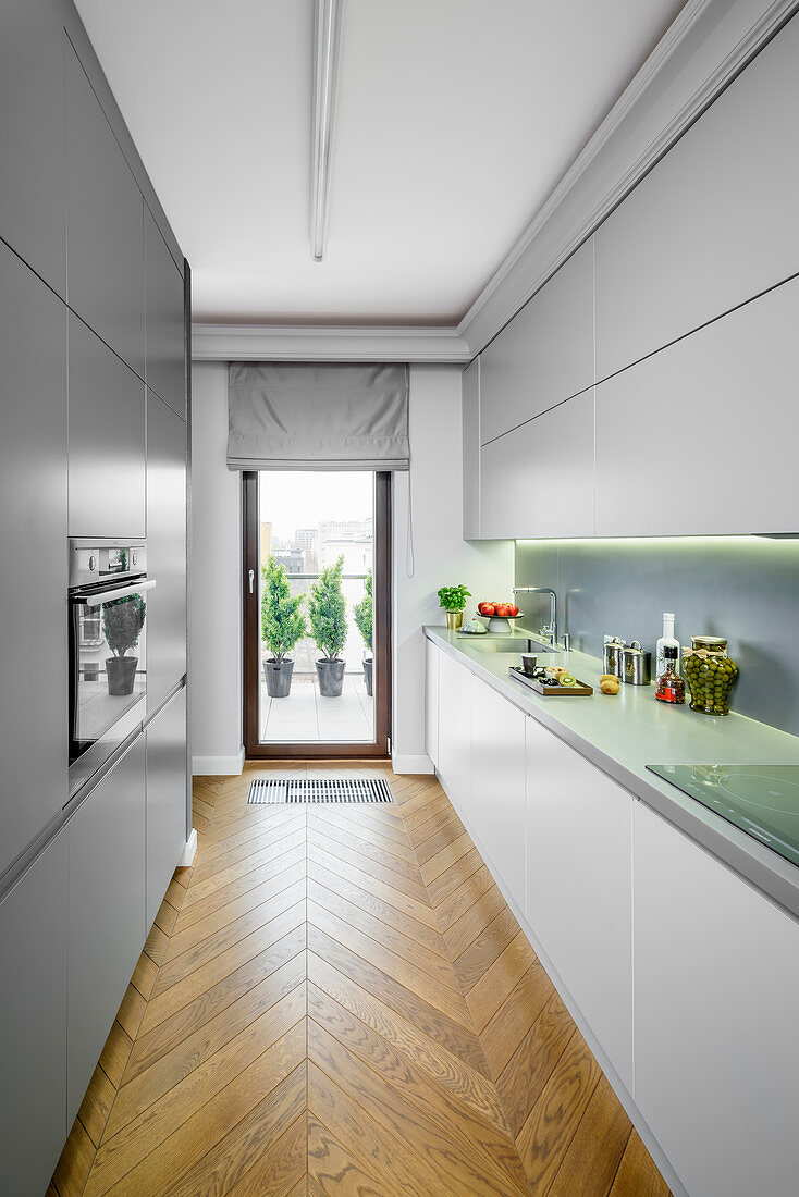 Narrow, grey, modern kitchen with balcony door and parquet flooring