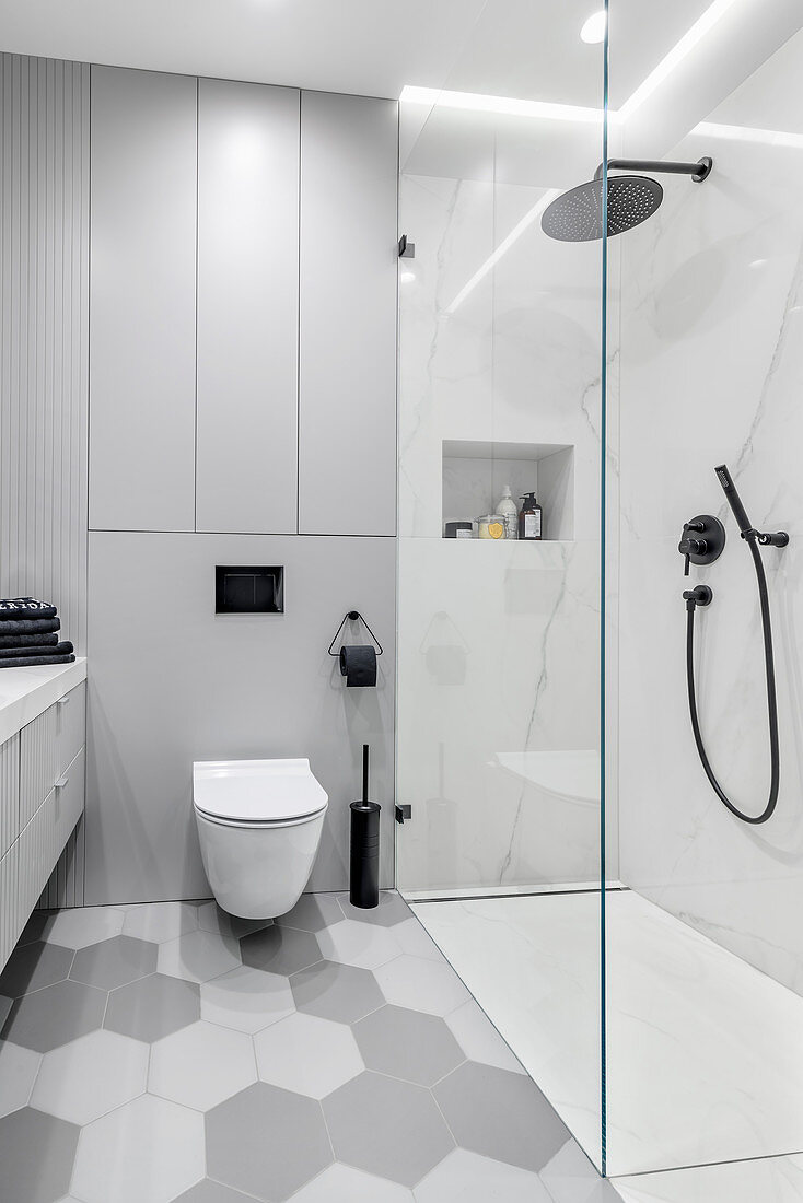 Duschbereich mit Glasabtrennung und Toilette in hellgrauem Badezimmer