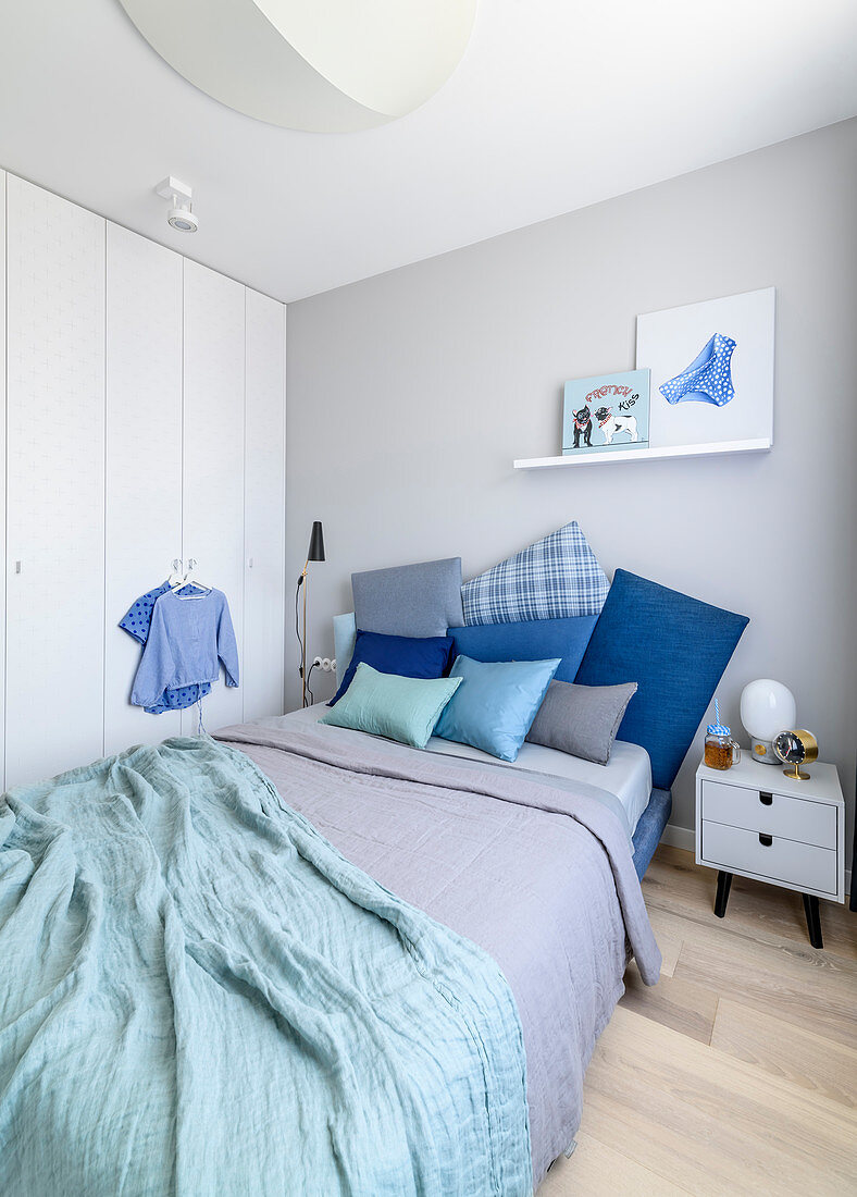 Kissen in Blautönen auf Doppelbett, Nachtkästchen und Einbauschrank im Schlafzimmer