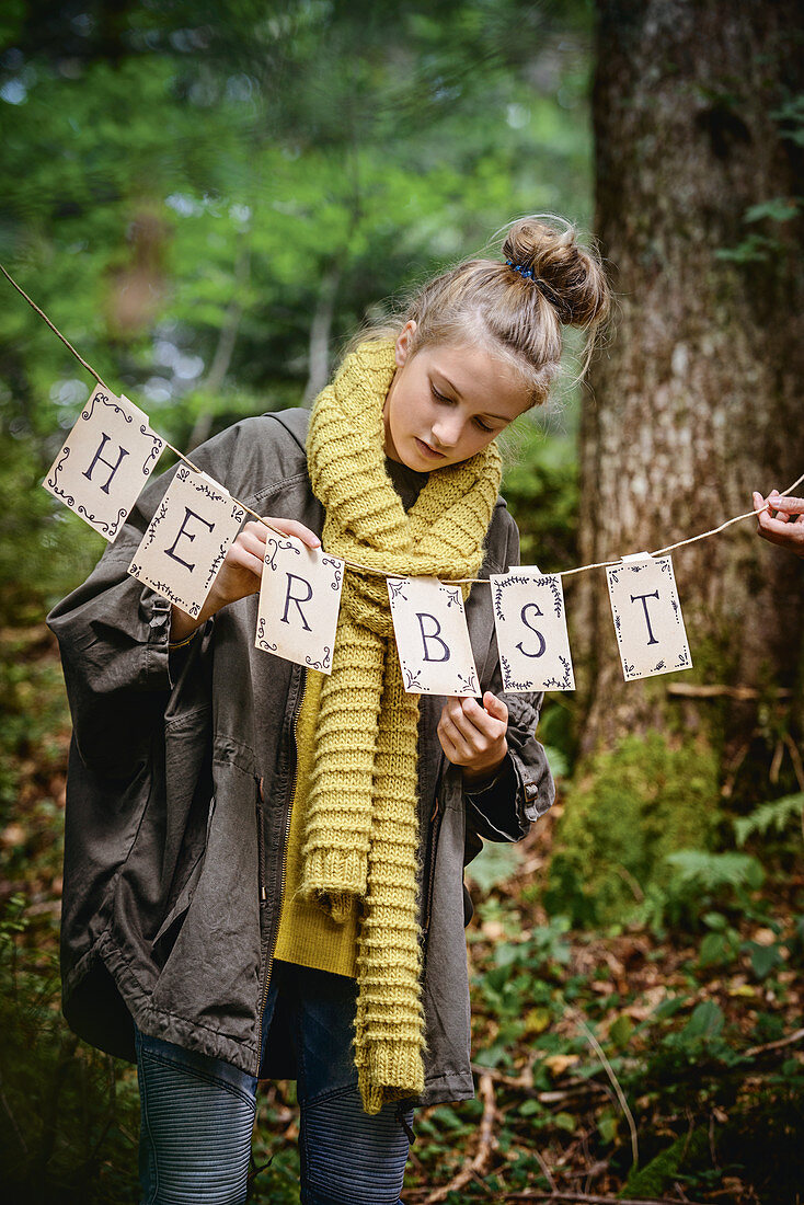 Mädchen hängt Herbstgirlande im Wald auf