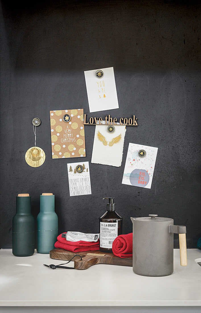Kitchen utensils on surface below notes and postcards pinned on black wall