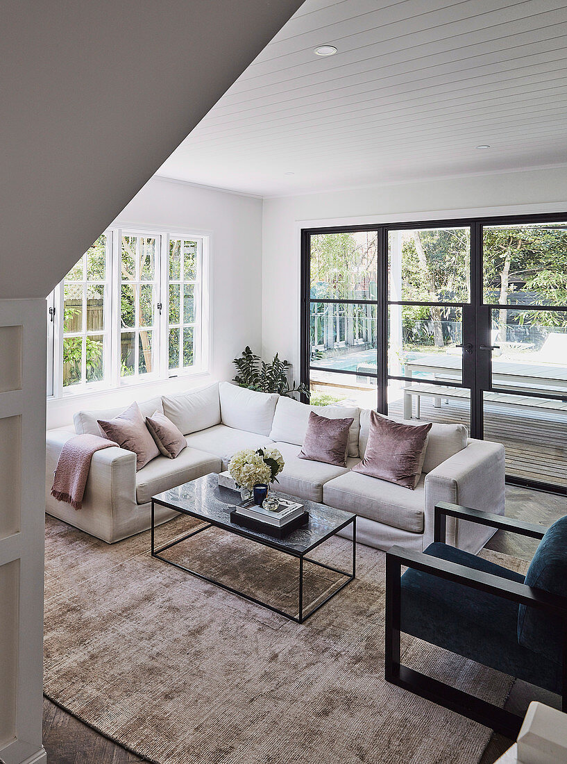 Blick ins Wohnzimmer mit weißem Sofa und Fensterfront zum Garten