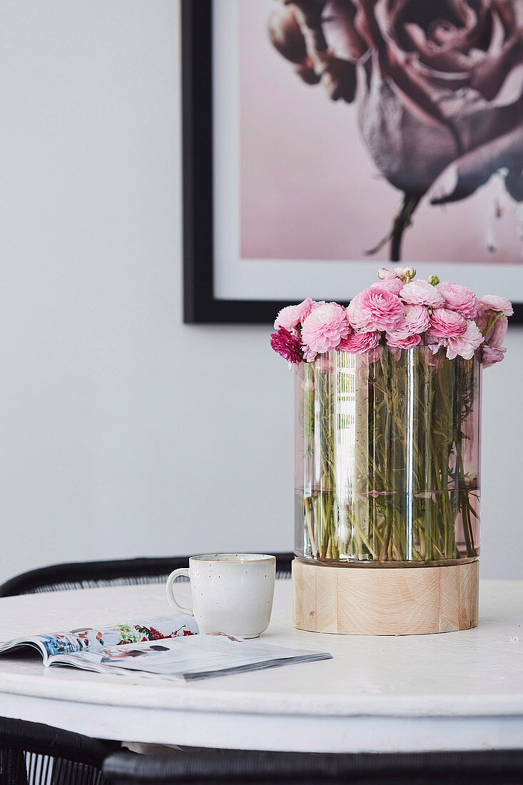 Pink ranunculus in a glass vase with wooden base on the table