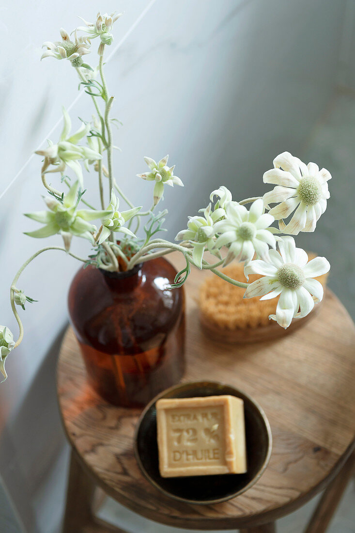 Blume in Apothekerflasche und Seife auf Holzhocker