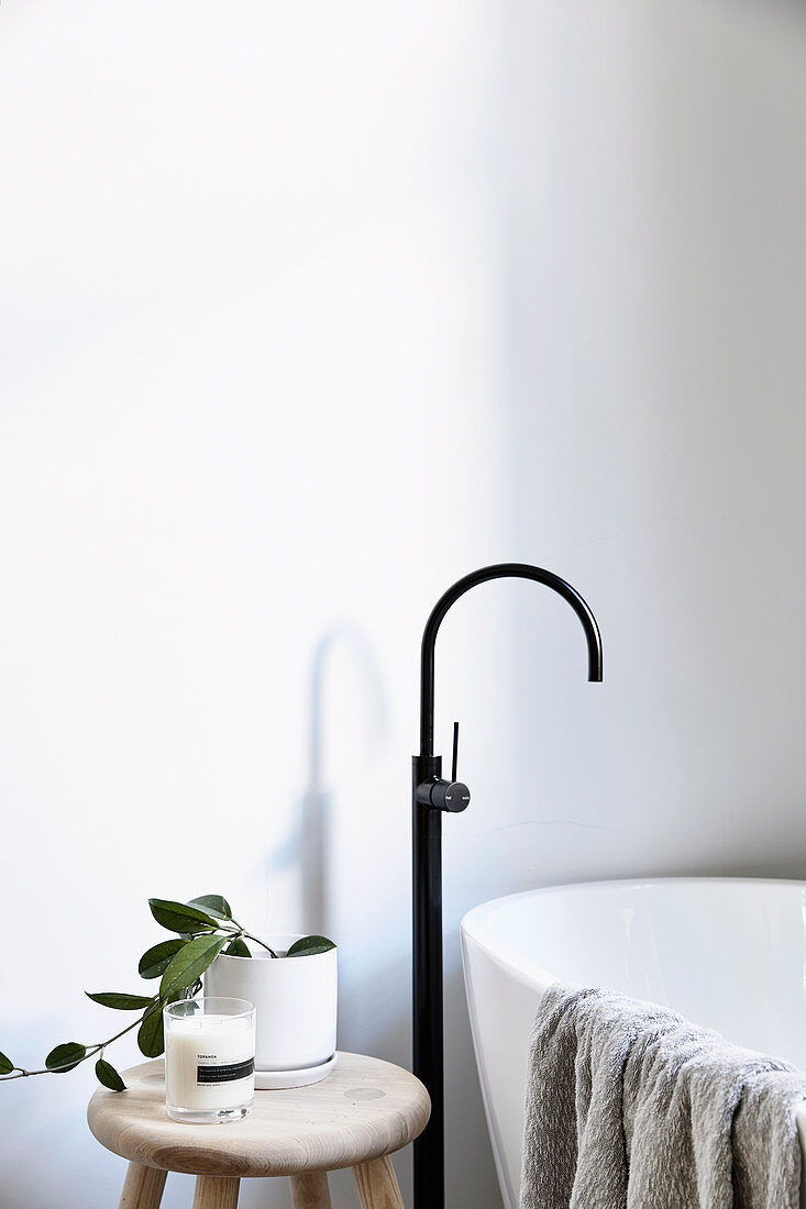 Wooden stool next to a modern free-standing bathtub with black fittings