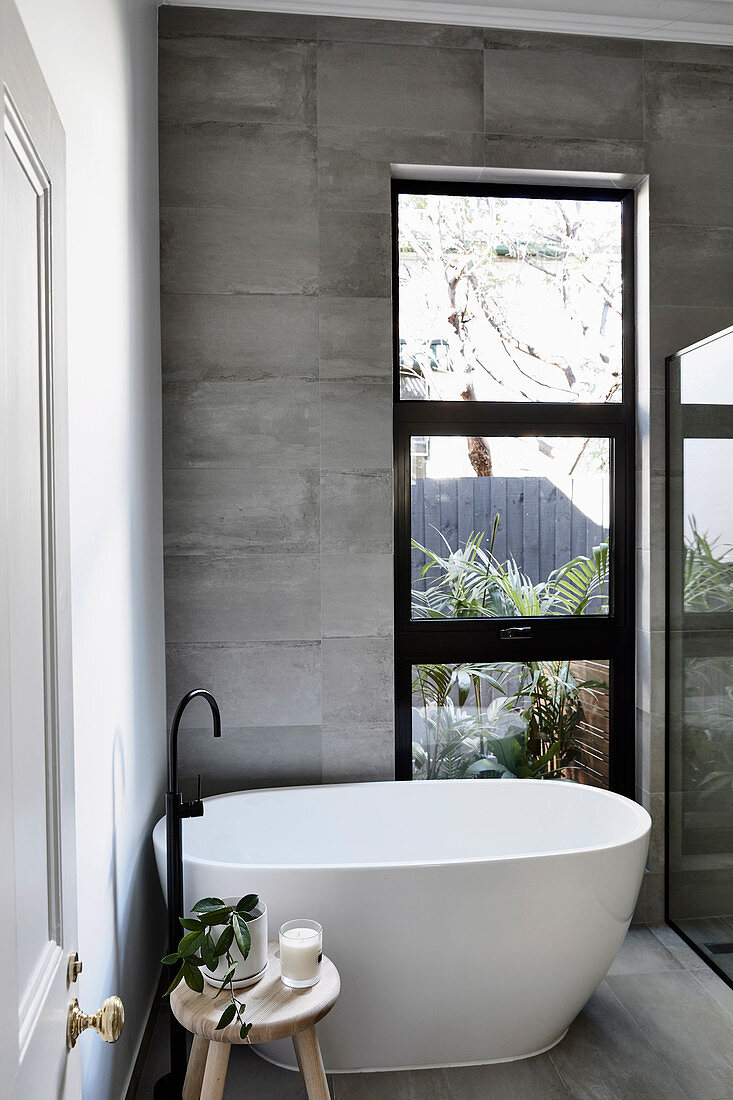 Modern freestanding bathtub by the window in a gray tiled bathroom