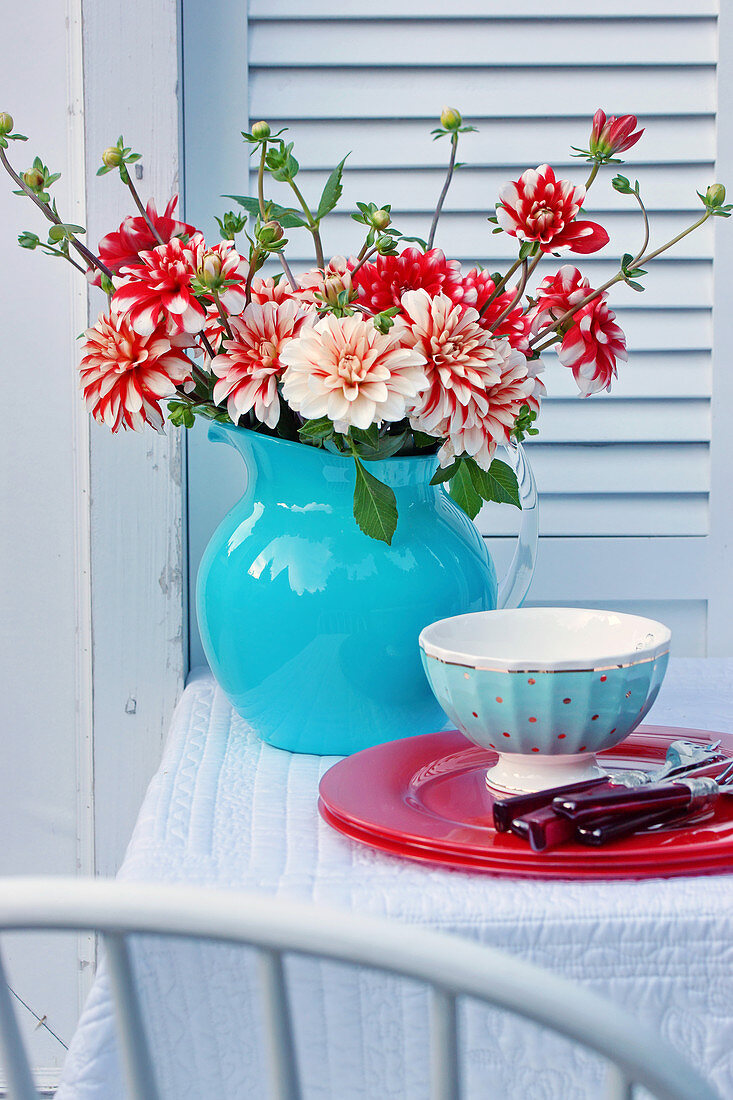 Bouquet of dahlias in blue jug and place setting on garden table