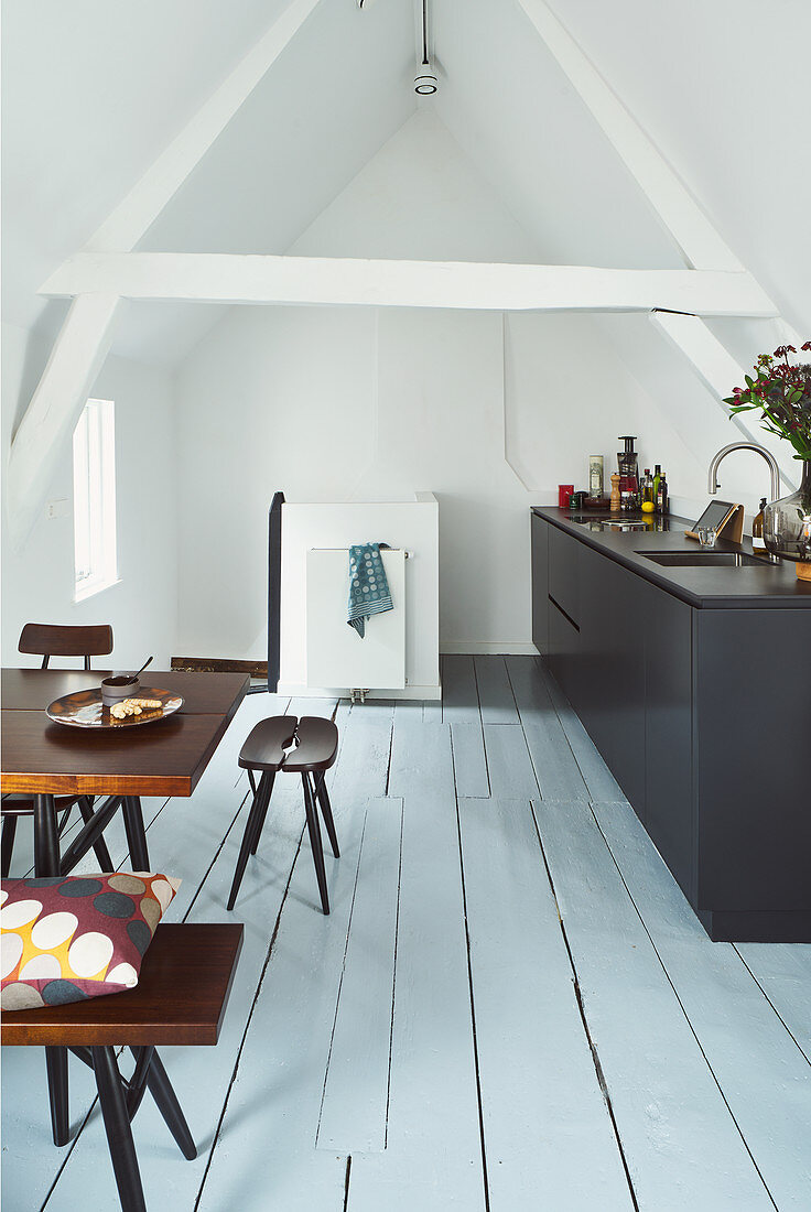 Schwarze Küchenzeile und Esstisch mit Sitzmöbeln in offenem Wohnraum unterm Dach