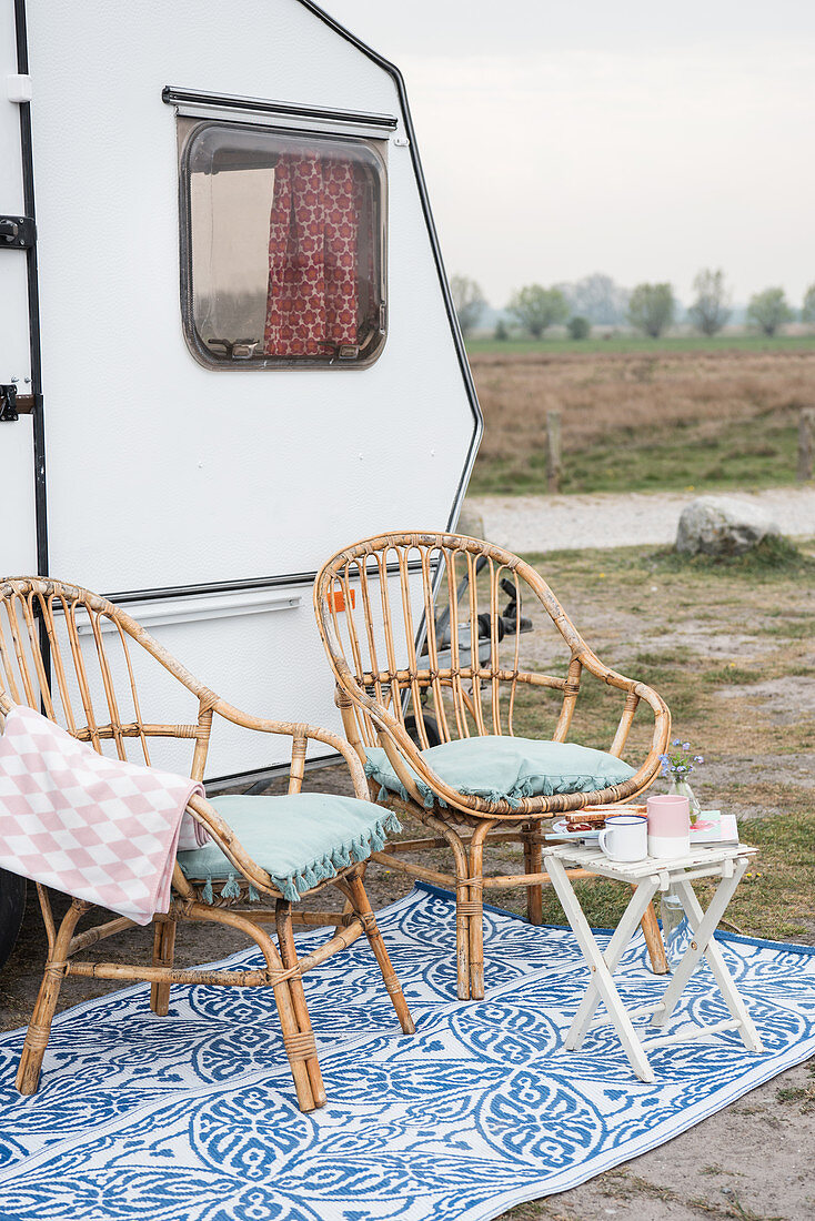 Two bamboo chairs and folding table outside renovated 80s caravan