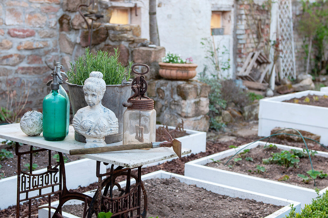 Bust of woman and vintage bottles on table next to freshly prepared raised beds in garden