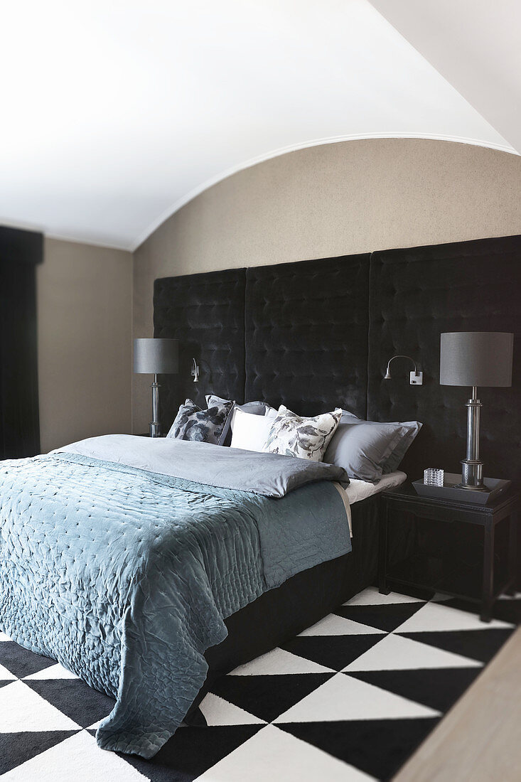 Double bed against black, button-tufted panel in bedroom with black-and-white rug