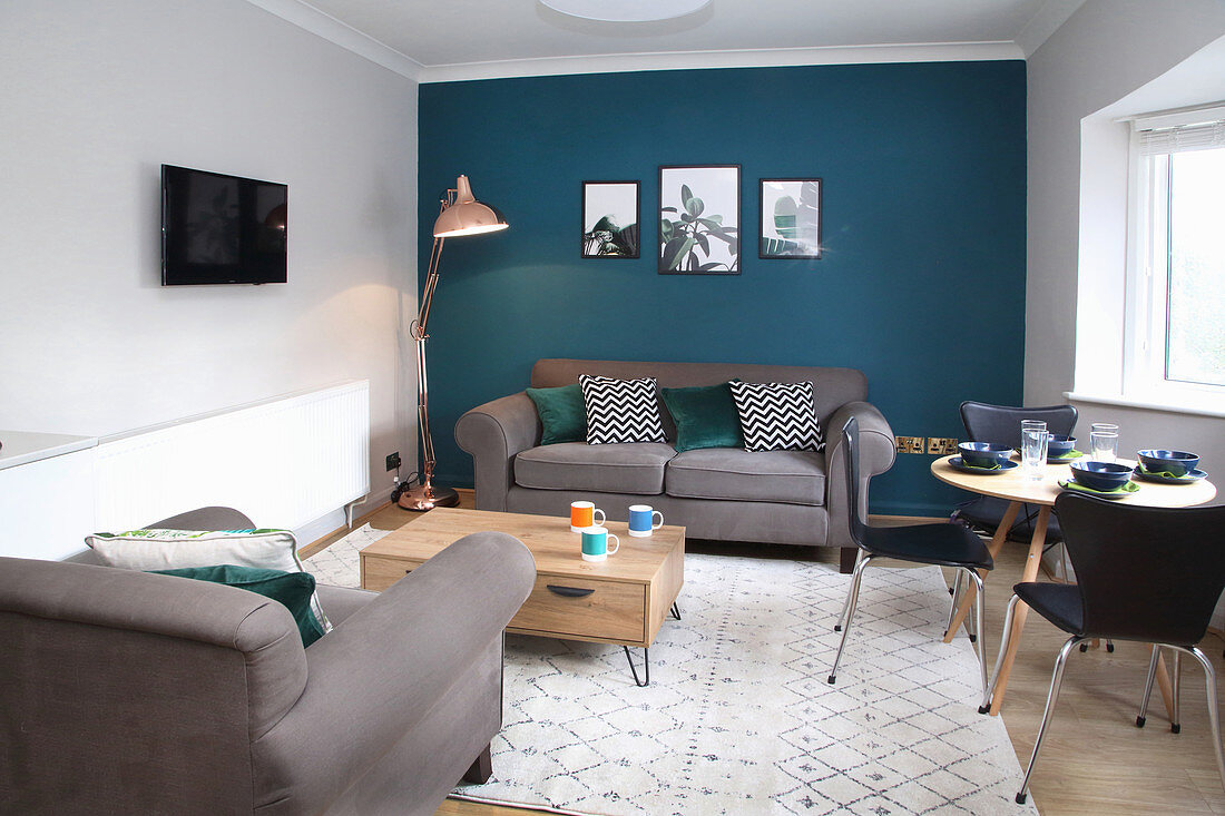 Graue Polstergarnitur und Esstisch mit Stühlen im Wohnzimmer mit petrolfarbener Wand