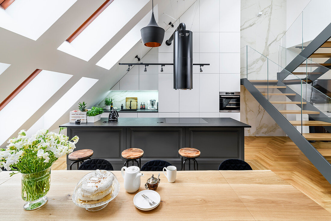 Blick über Esstisch auf Kücheninsel und Treppe in hohem Raum mit Dachschräge