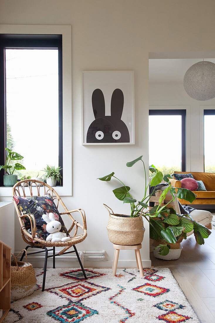 Rattan chair and Swiss cheese plant on colourful ethnic rug below picture with rabbit motif