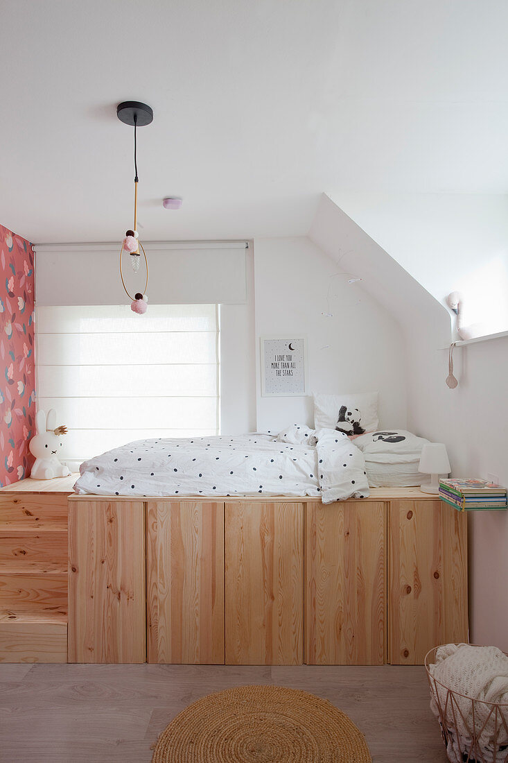 Child's bed on platform made from wooden cupboards with steps