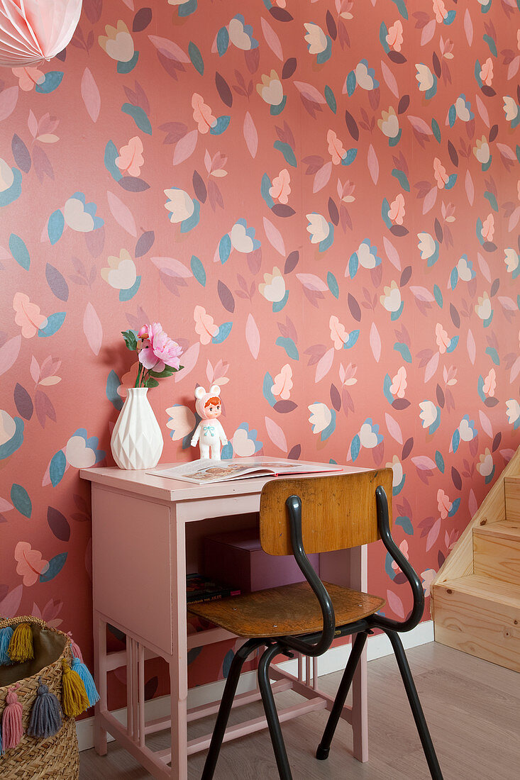 Alter Stuhl und rosafarbenes Tischchen vor rot geblümter Tapete