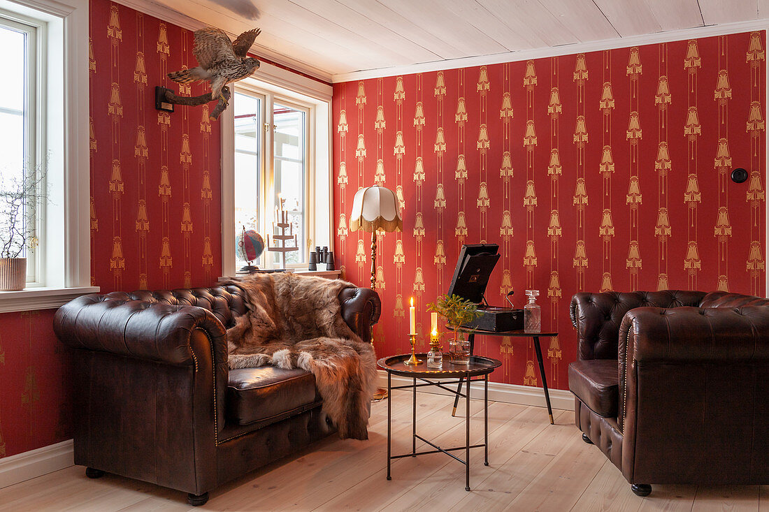 Chesterfield sofa and armchair around side table in room with red wallpaper