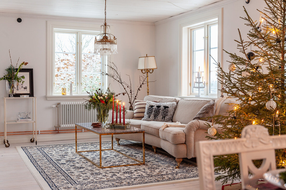 Geschmückter Weihnachtsbaum, helle Couch und Couchtisch im Wohnzimmer