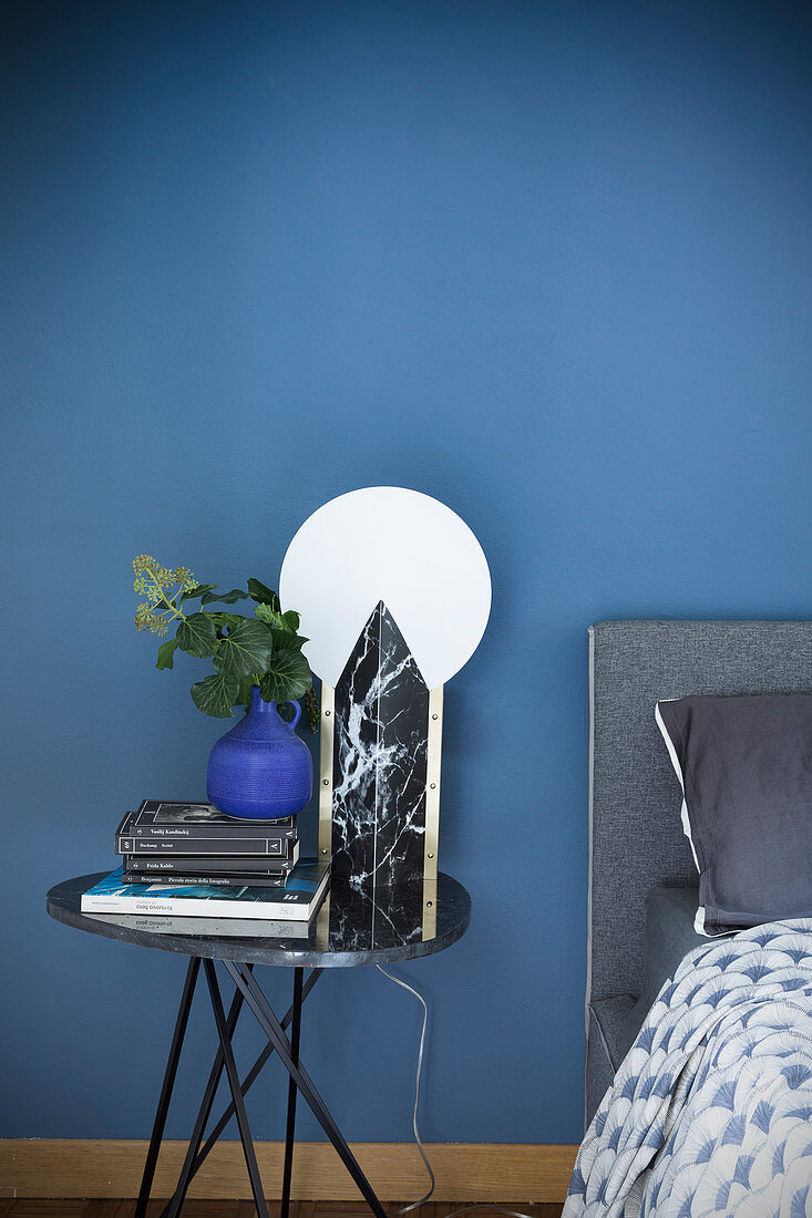 Tischleuchte aus schwarzem Marmor vor blauer Wand im Schlafzimmer