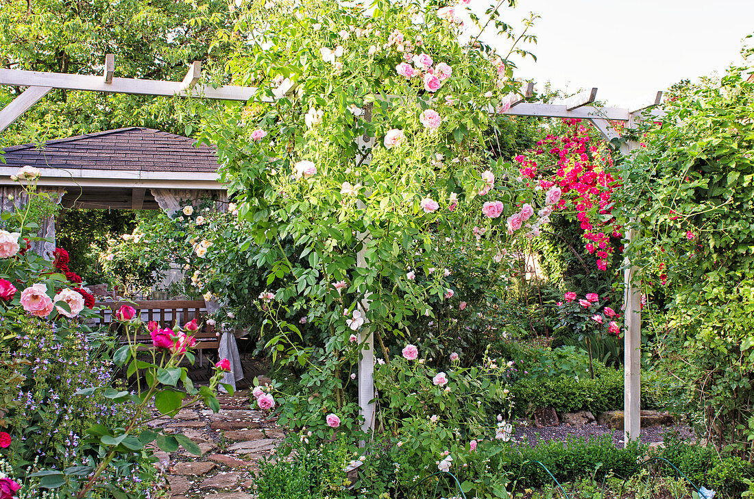 Gartensezene mit blühenden Rosen und Pavillon mit Sitzecke