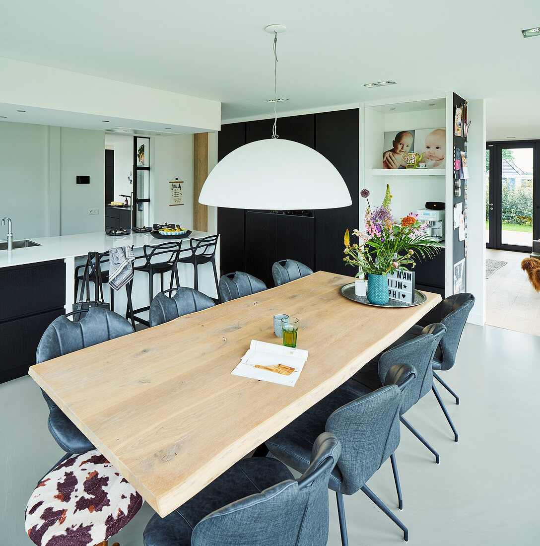 Oak dining table in open-plan interior with black-and-white kitchen in background