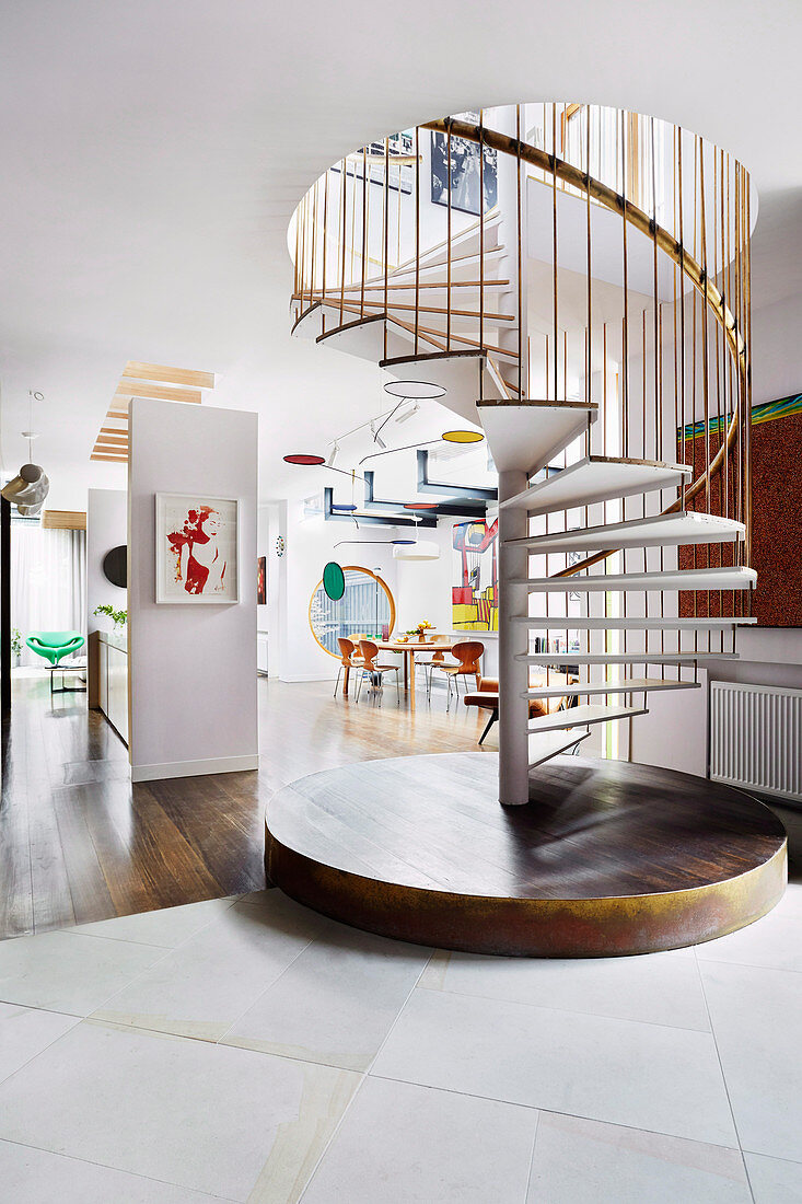 Spiral staircase with a brass-colored railing in the open living room of a designer apartment
