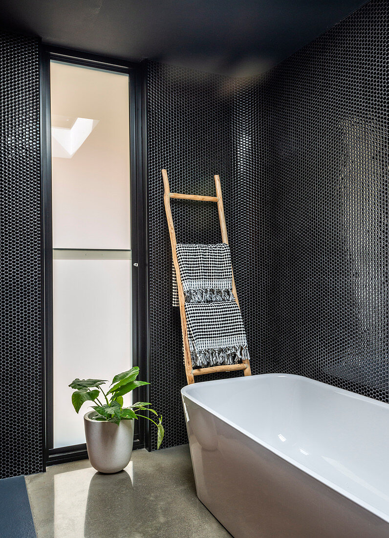 Moderne freistehende Badewanne in Bad mit schwarzen Wänden und Milchglasfenstern