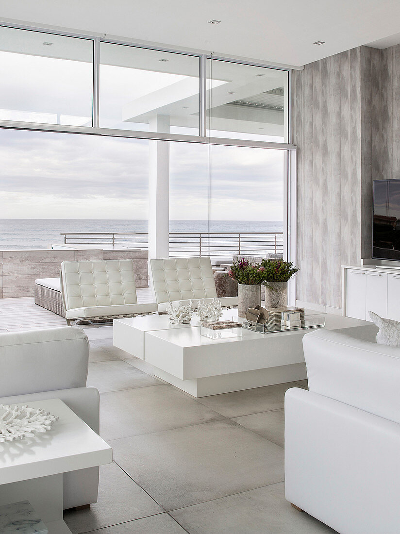 Modern living room decorated entirely in white with sea view through glass wall