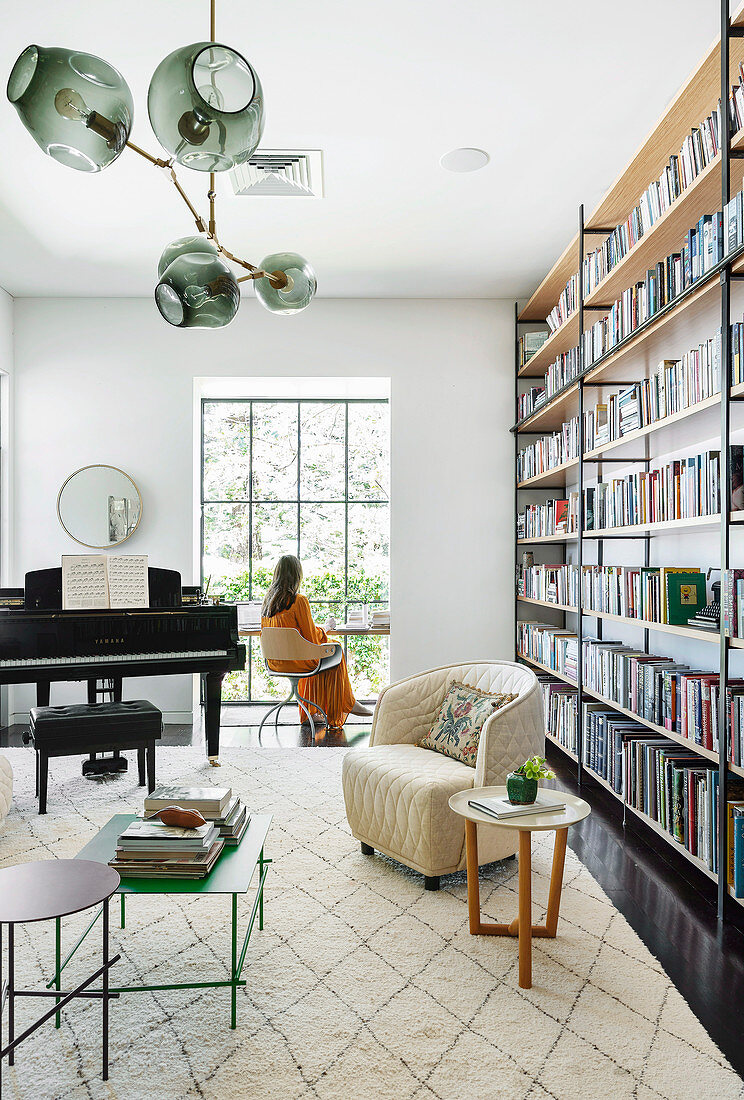 Wohnzimmer mit deckenhoher Bücherwand, Klavier und Schreibtisch im modernen Erker