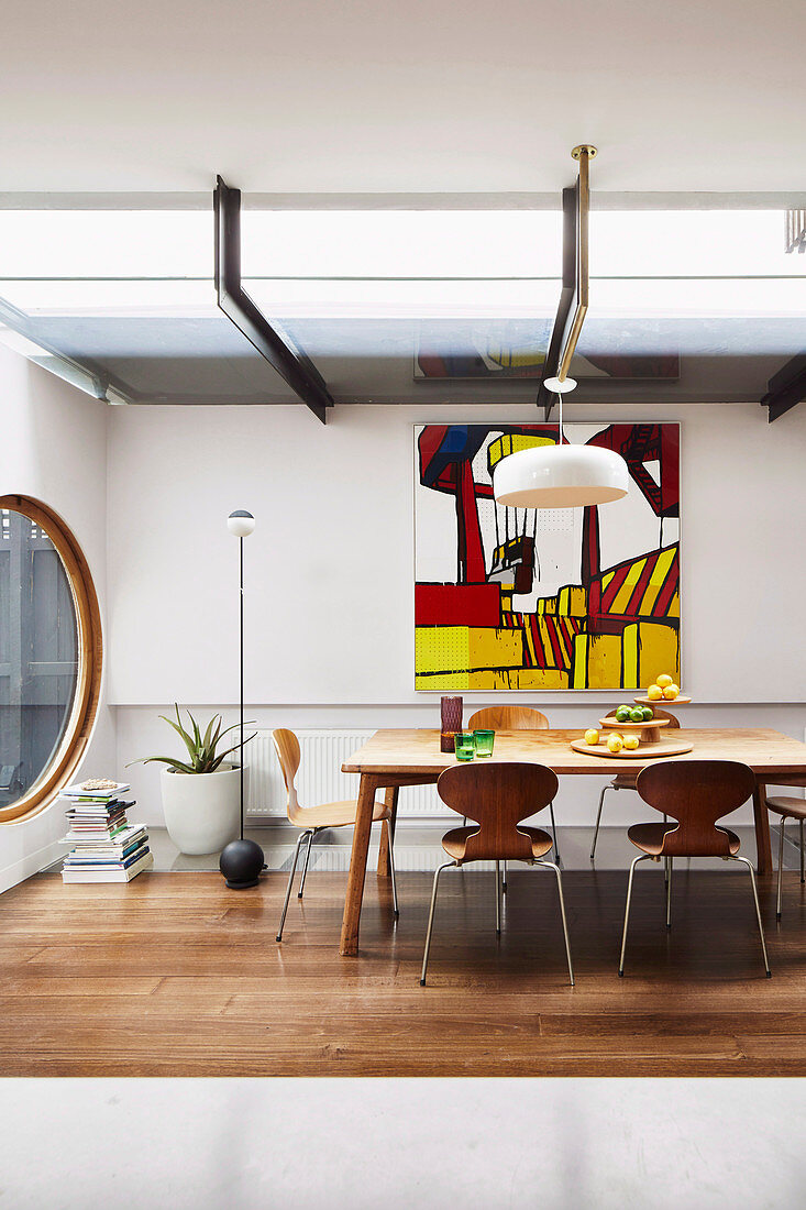 Dining area in designer apartment with dining table, round window and abstract wall painting
