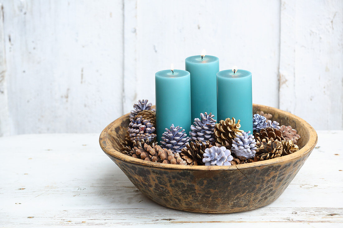 Elegant Christmas arrangement of blue pillar candles and pine cones dipped in coloured wax in bowl