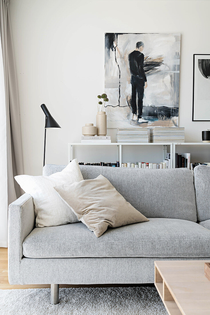 Graues Sofa vor halbhohen Regalen mit Zeitschriften und Gemälde