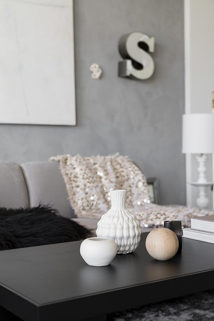 Vases and ornamental spheres on black coffee table in living room in shades of grey