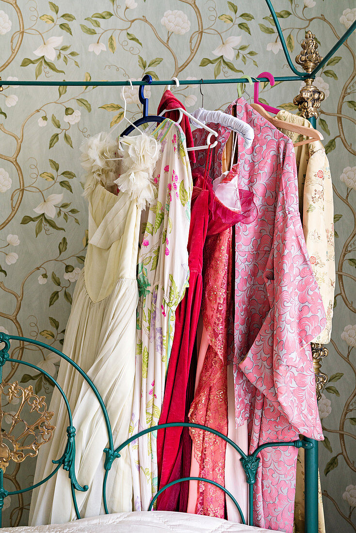 Women's clothing hung from metal frame of ornate four-poster bed