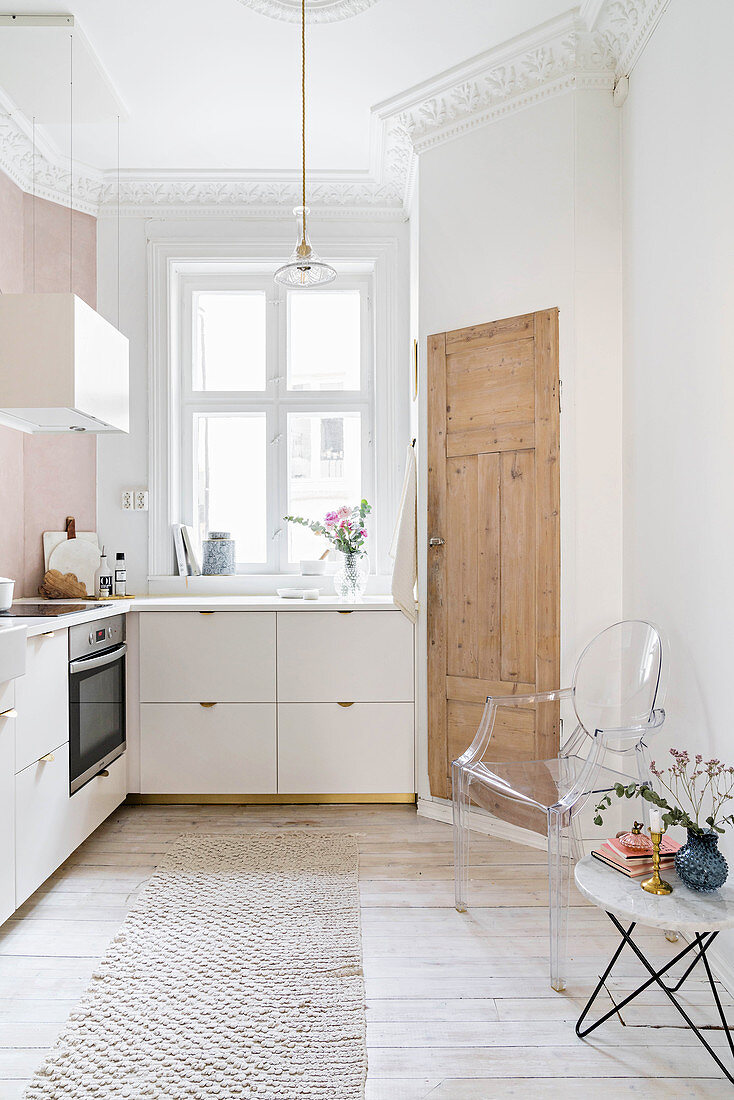 Weiße Einbauküche mit Stuckdecke und Holzdielenboden, Beistelltisch und Klassikerstuhl