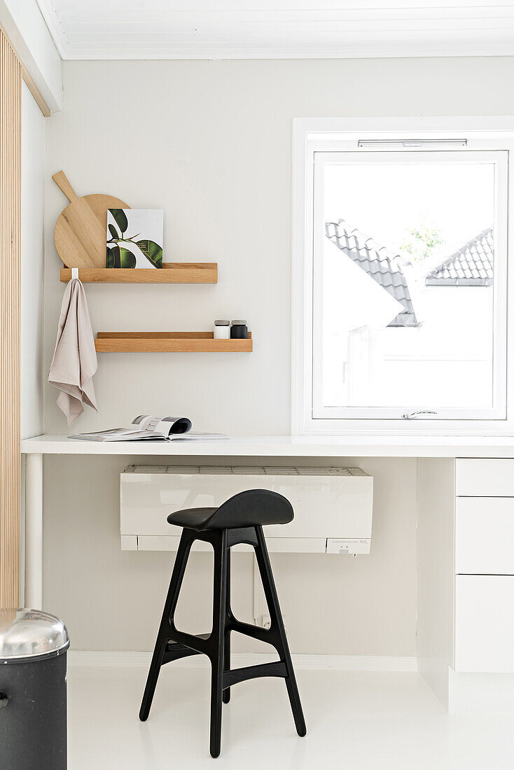 Wooden shelves on wall and white table with stool below window in corner of kitchen