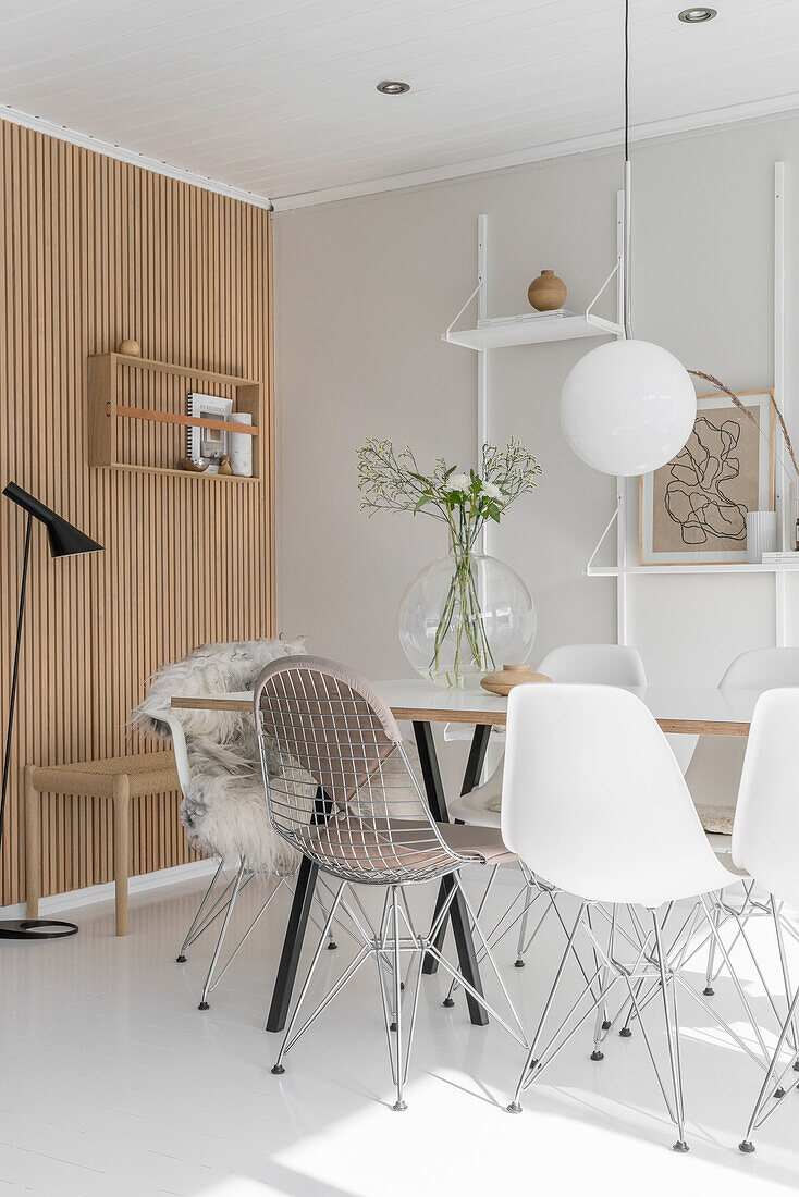 Dining table and various Eames chairs in white interior with wooden elements