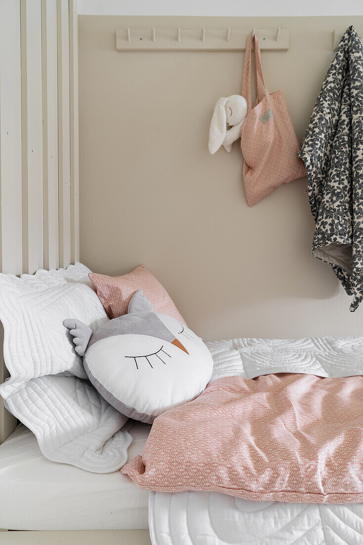 Bed with owl-shaped pillow and pink-and-white bed linen in girl's bedroom