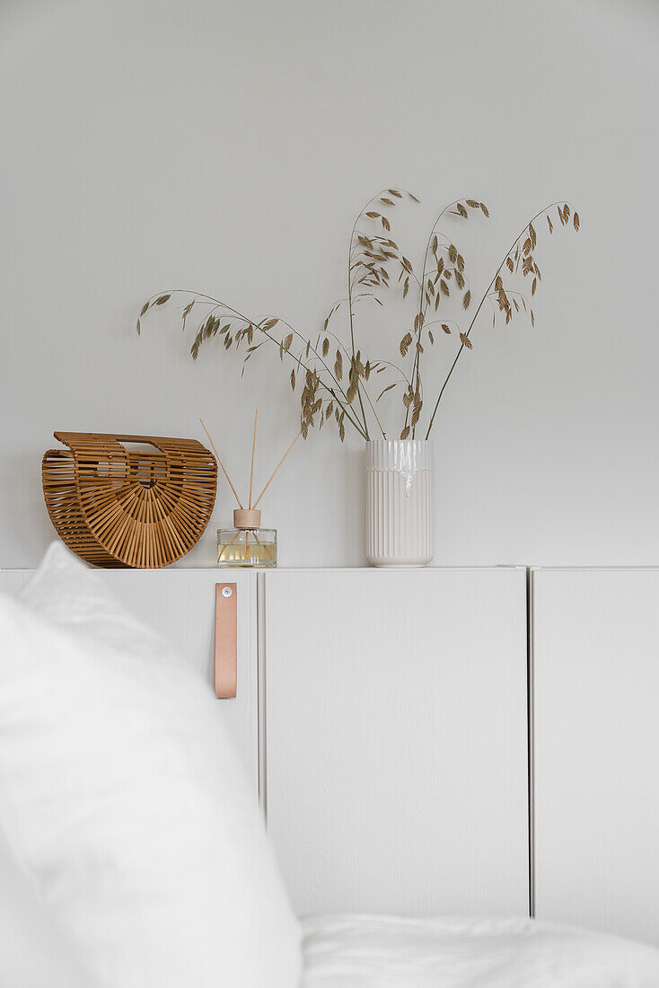 Tasche, Raumduft und Vase auf weißem Sideboard in Schlafzimmer